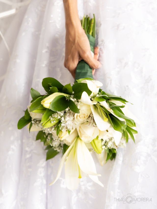 Detalhe do buquê de copos-de-leite segurado pela noiva, com a renda do vestido ao fundo
