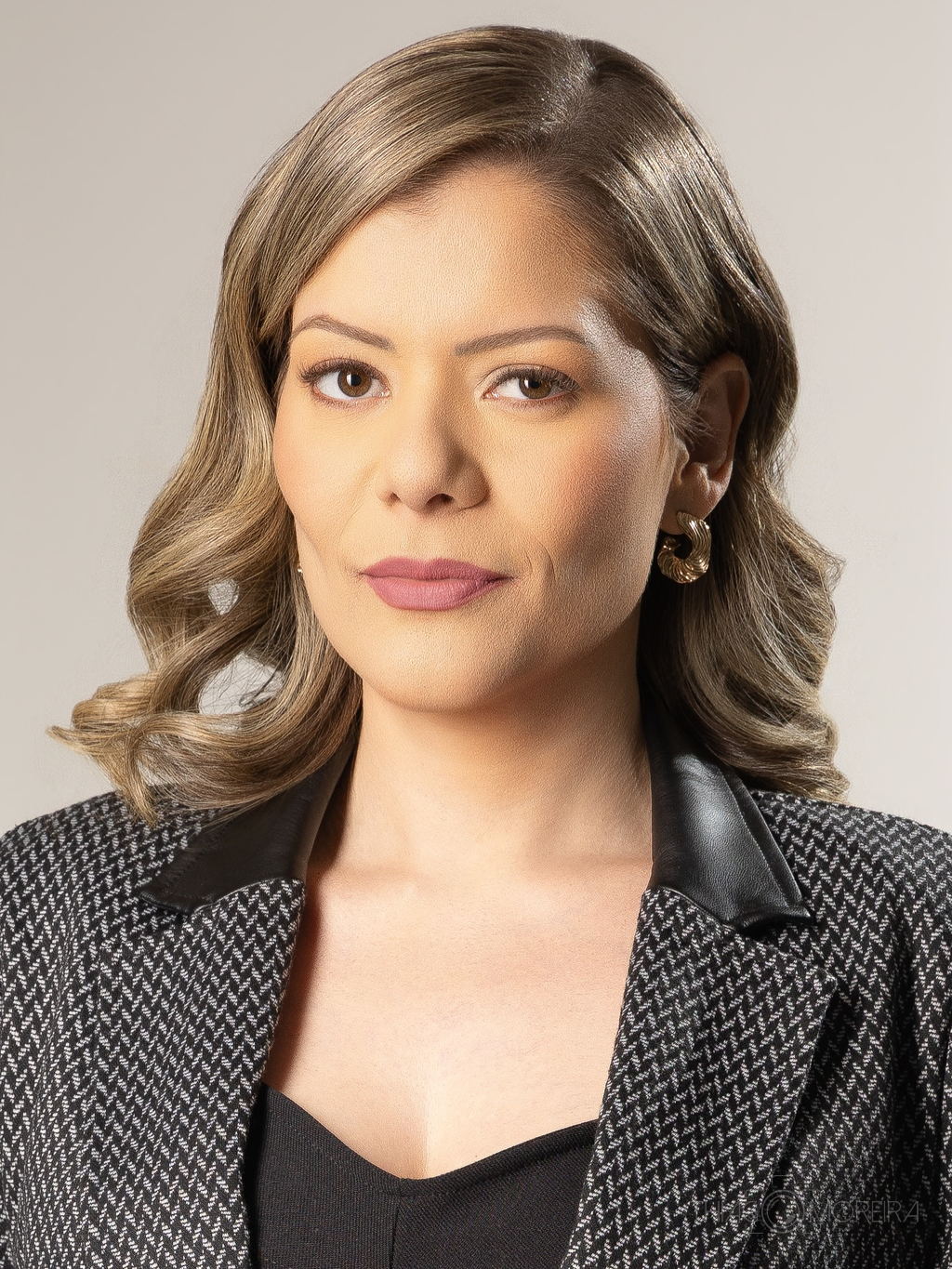 Retrato corporativo de uma mulher de blazer xadrez sobre fundo liso cinza-claro, com enquadramento fechado no rosto
